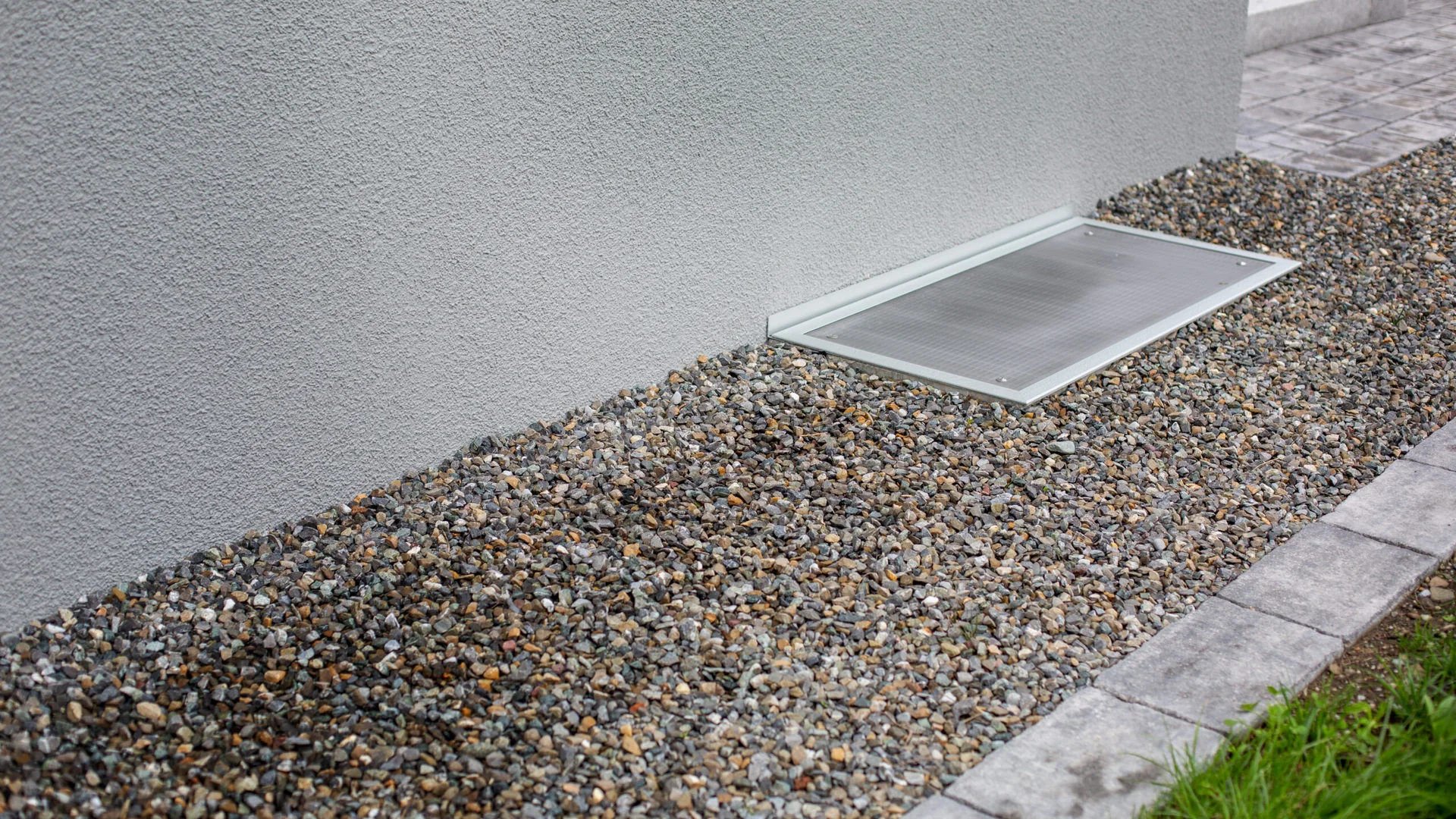 Lichtschachtabdeckung im Kiesbett vor der Hauswand